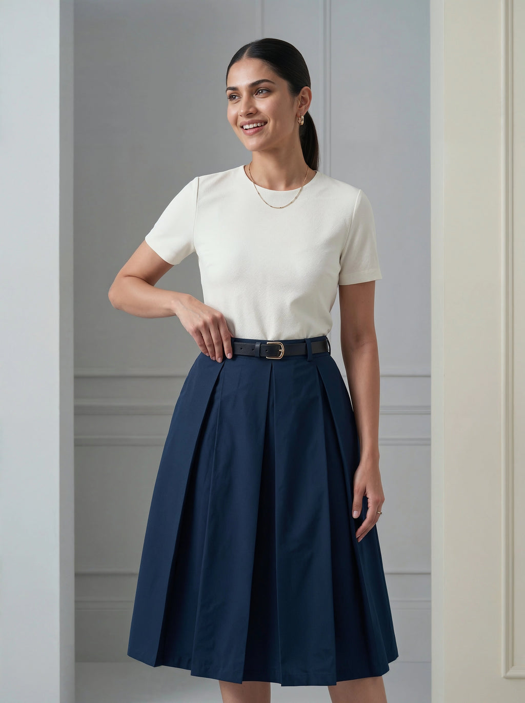 Woman wearing a white top and navy skirt against a gray wall.