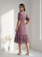 Woman standing indoors wearing a textured plum colored tiered dress