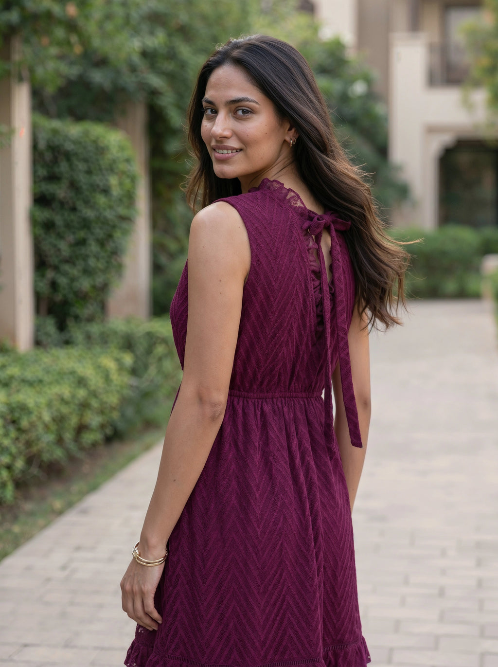 Woman in a purple dress standing outdoors on a path with greenery.
