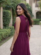 Woman in a purple dress standing outdoors on a path with greenery.