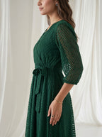 Woman wearing a green dress with sheer sleeves against a white curtain background
