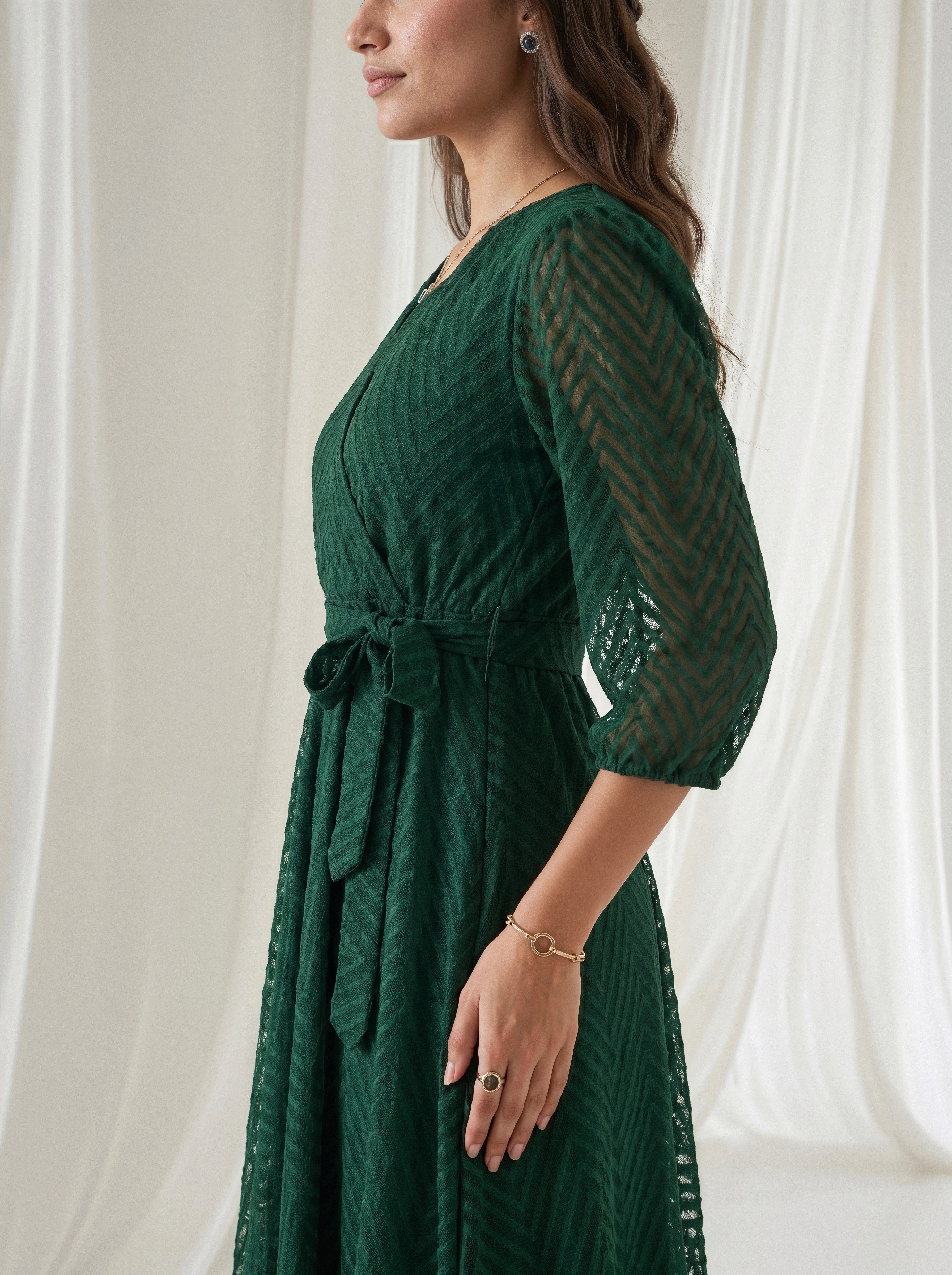 Woman wearing a green dress with sheer sleeves against a white curtain background