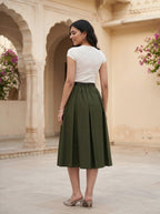 Woman wearing a white top and green skirt standing in front of architectural arches with floral decorations.
