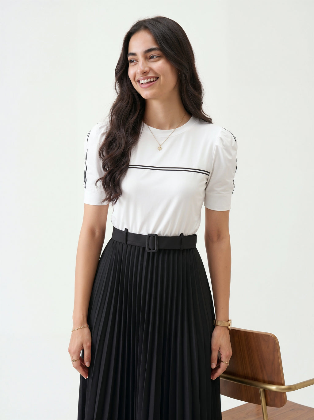 Woman wearing a white T-shirt with black trim and a black pleated skirt on a white background