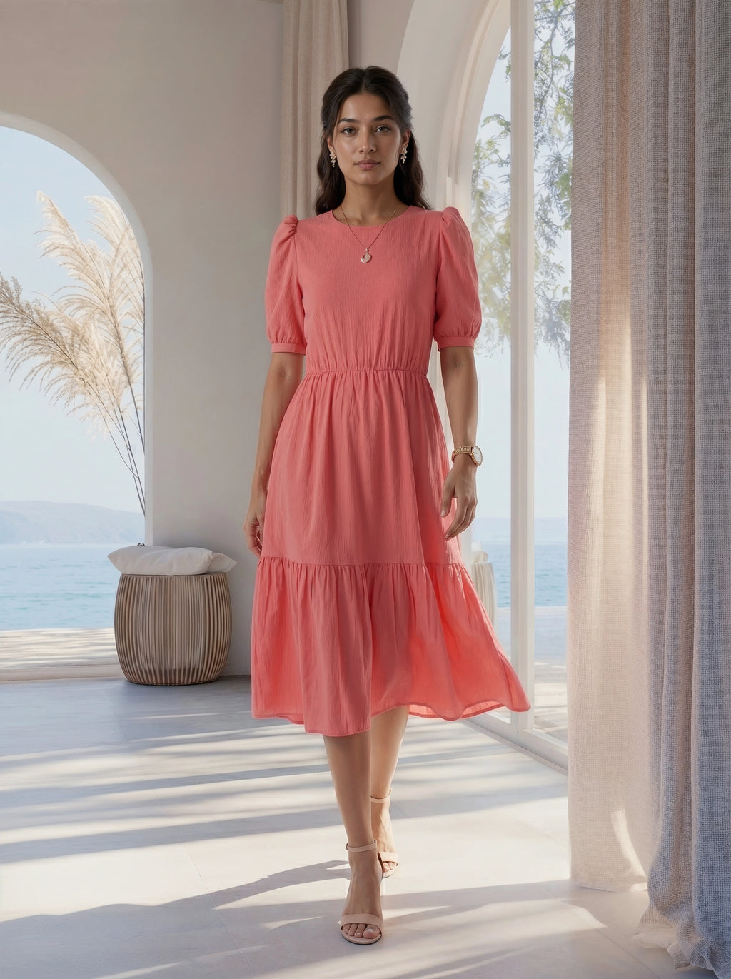 Woman in a pink dress standing in a bright room with large windows and natural light.