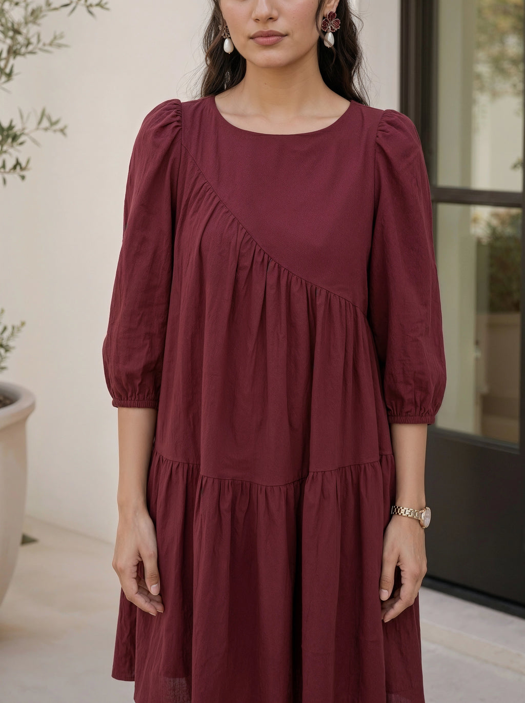 Woman wearing a burgundy dress with puffed sleeves in an indoor setting.