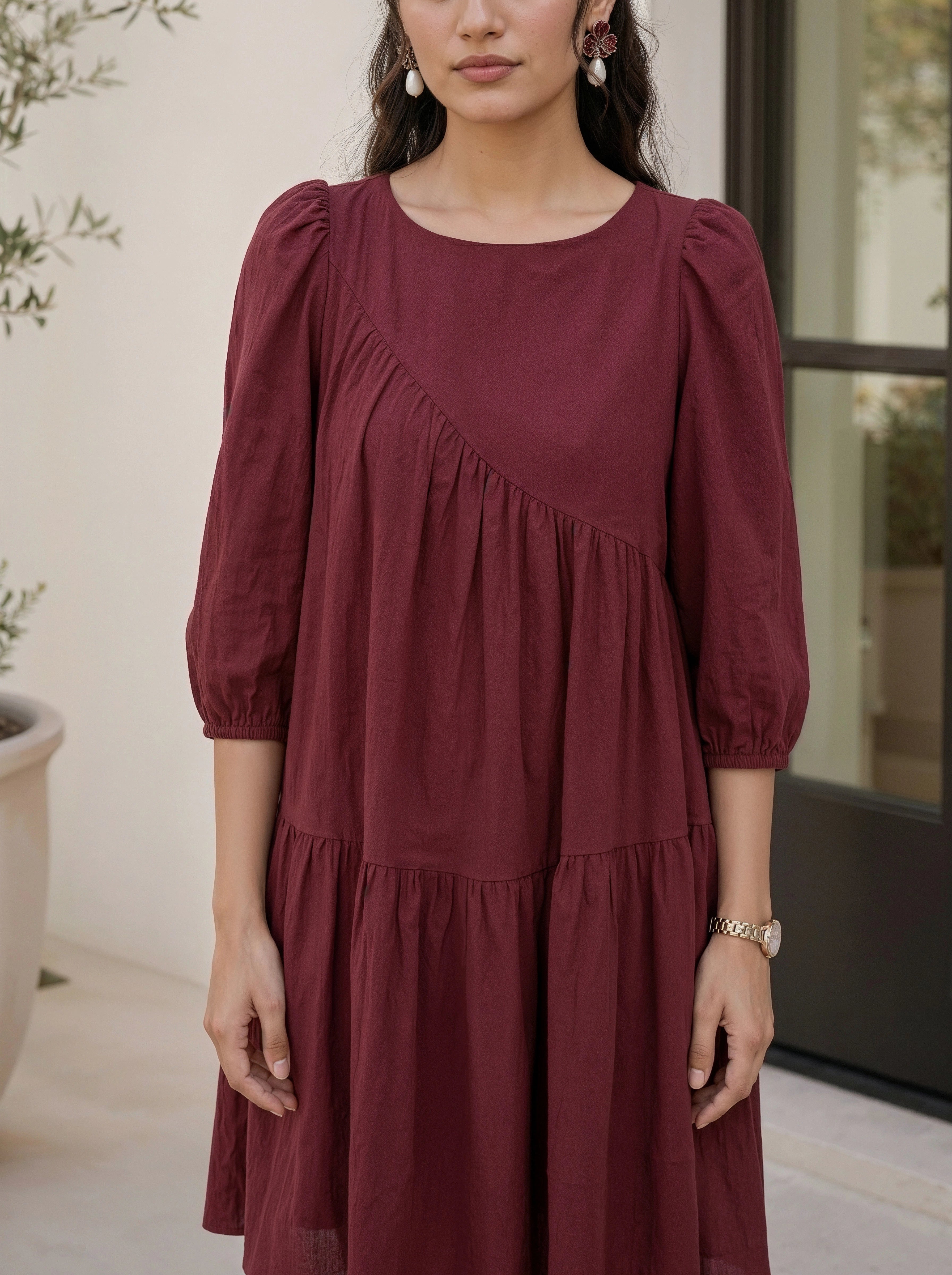 Woman wearing a burgundy dress with puffed sleeves in an indoor setting.