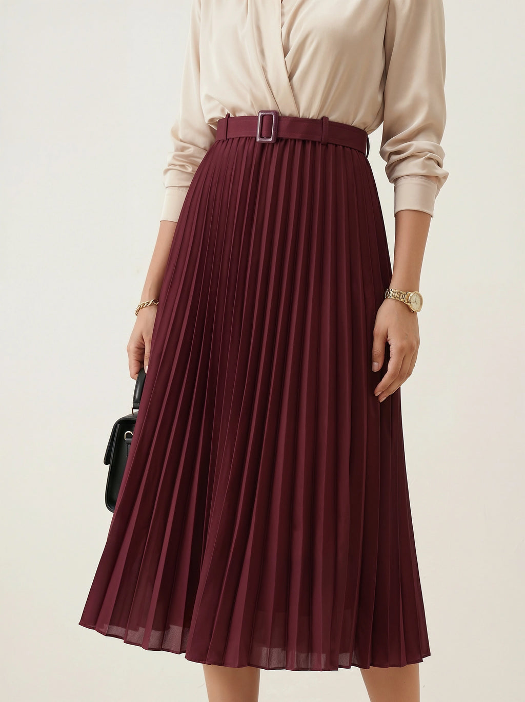 Person wearing a beige top and burgundy pleated skirt on a plain background