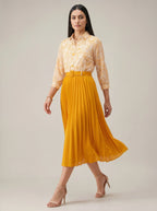 Woman wearing a yellow floral shirt and mustard yellow skirt on a plain background
