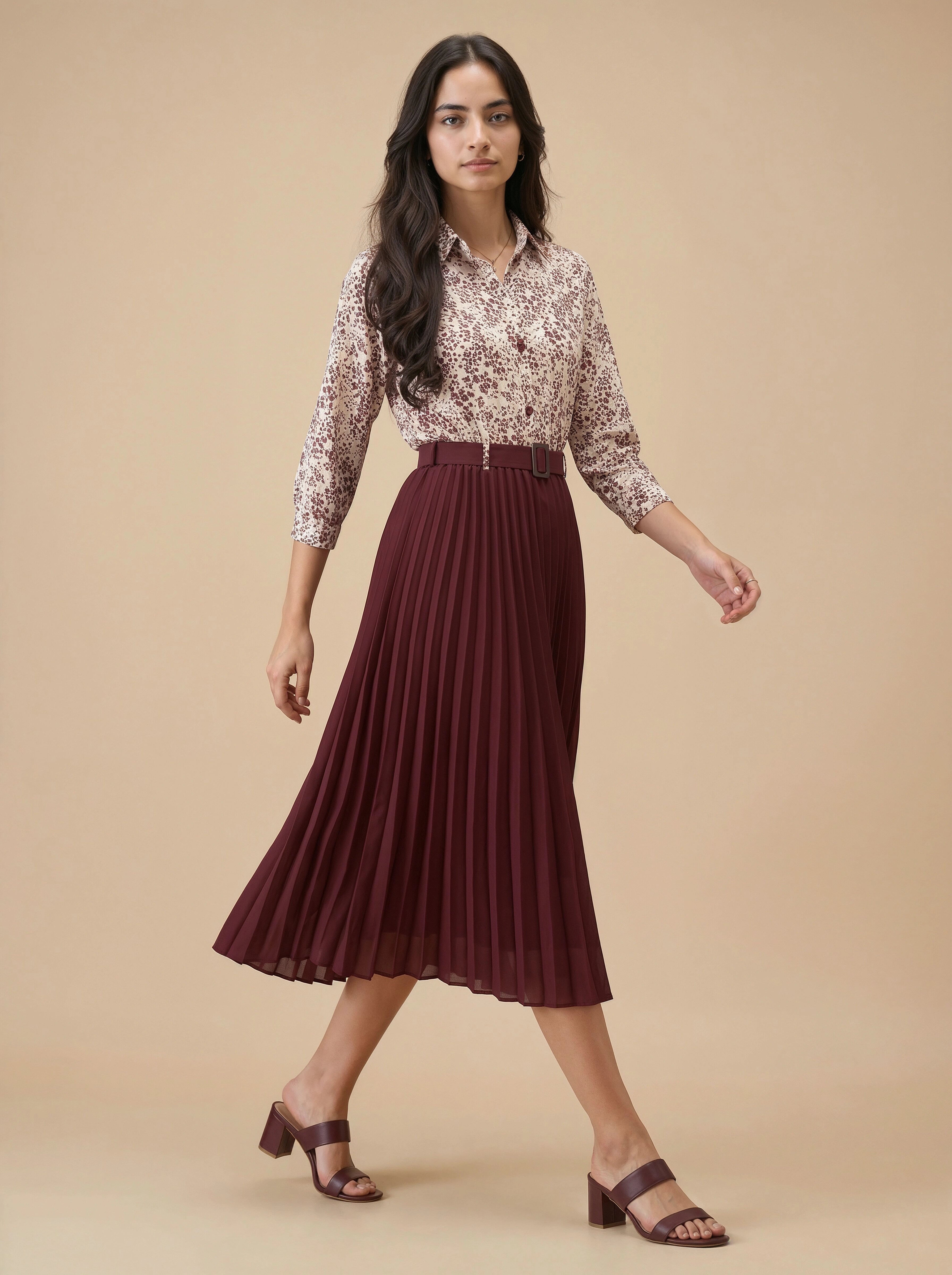 Woman wearing a patterned blouse and maroon pleated skirt on a beige background