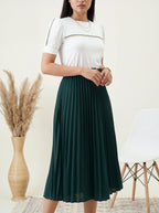 Woman wearing a white top and green skirt standing in a room with decorative elements.