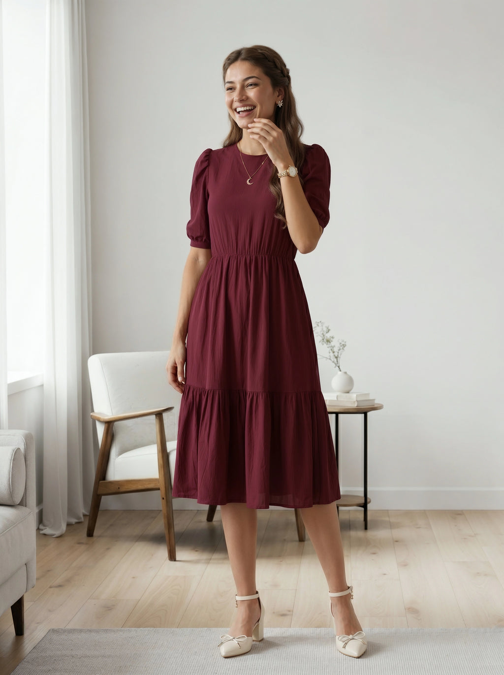 Woman in a burgundy dress standing in a room with light-colored walls and wooden flooring.