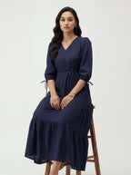 Woman wearing a navy blue dress sitting on a wooden stool against a white background