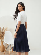 Woman wearing a white top and navy skirt in a minimalistic room.