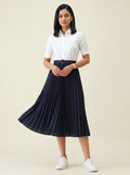 Woman wearing a white shirt and navy pleated skirt on a beige background