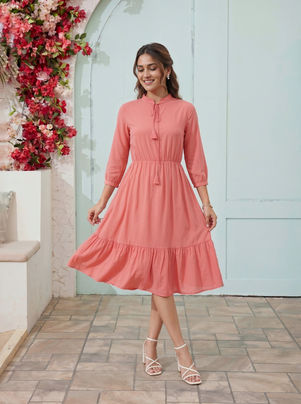 Woman in a pink dress standing in front of a decorative floral wall and light blue door.