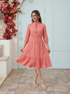 Woman in a pink dress standing in front of a decorative floral wall and light blue door.