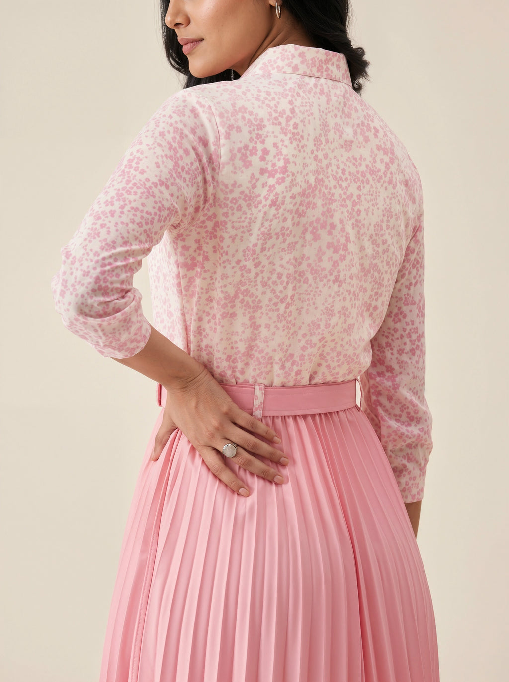 Woman wearing a pink floral blouse and pleated skirt against a beige background