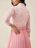 Woman wearing a pink floral blouse and pleated skirt against a beige background