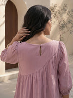 Woman wearing a pink blouse with a textured back design, standing outdoors.