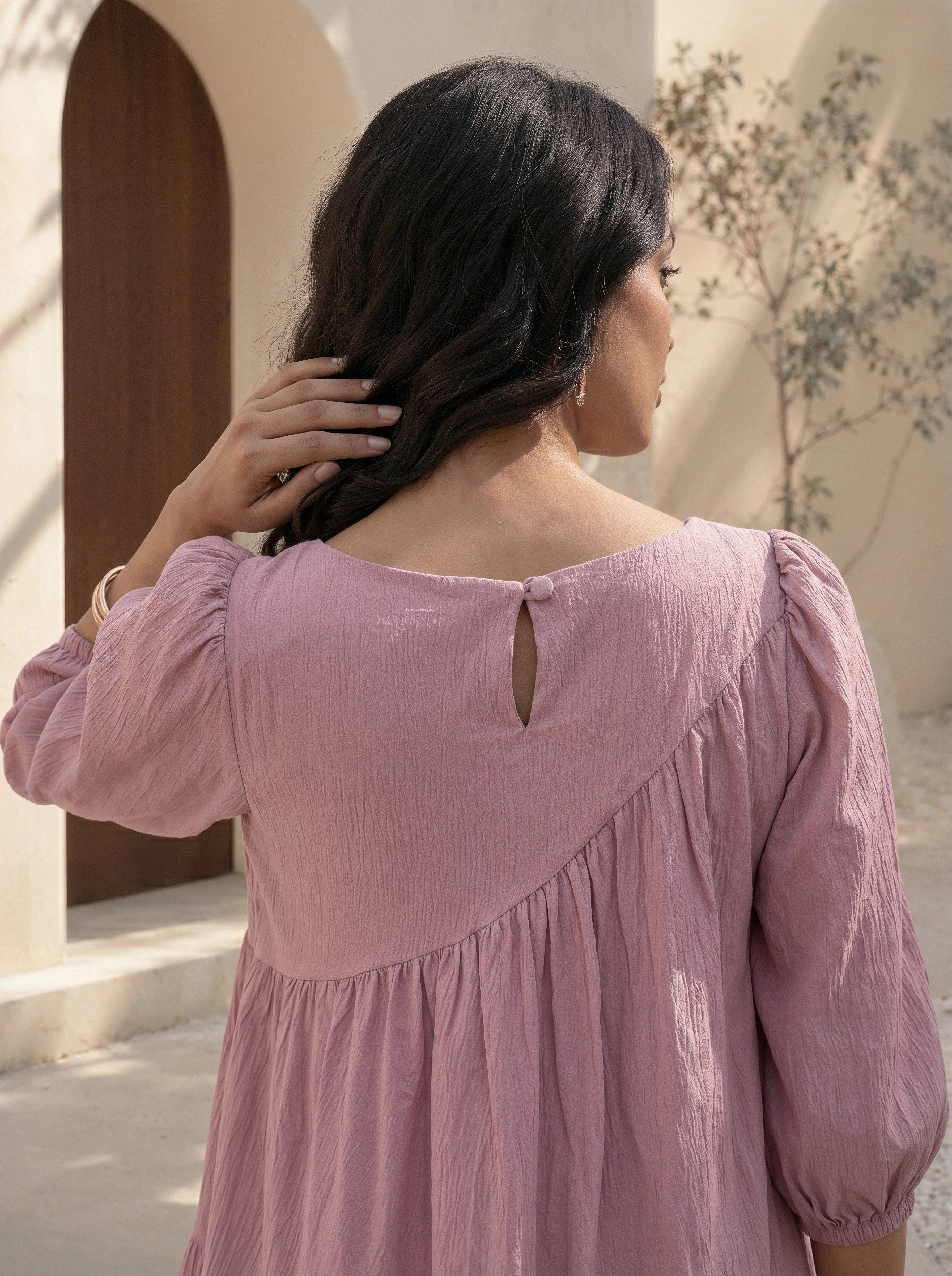 Woman wearing a pink blouse with a textured back design, standing outdoors.