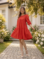 Woman in a red dress standing on a stone path with flowers and a house in the background