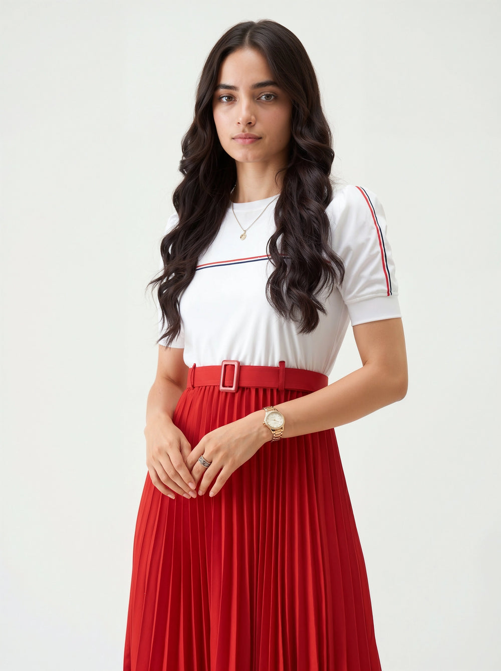 Woman wearing a white top with red and blue accents and a red pleated skirt on a white background