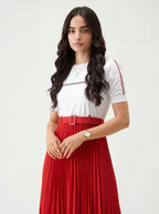 Woman wearing a white top with red and blue accents and a red pleated skirt on a white background