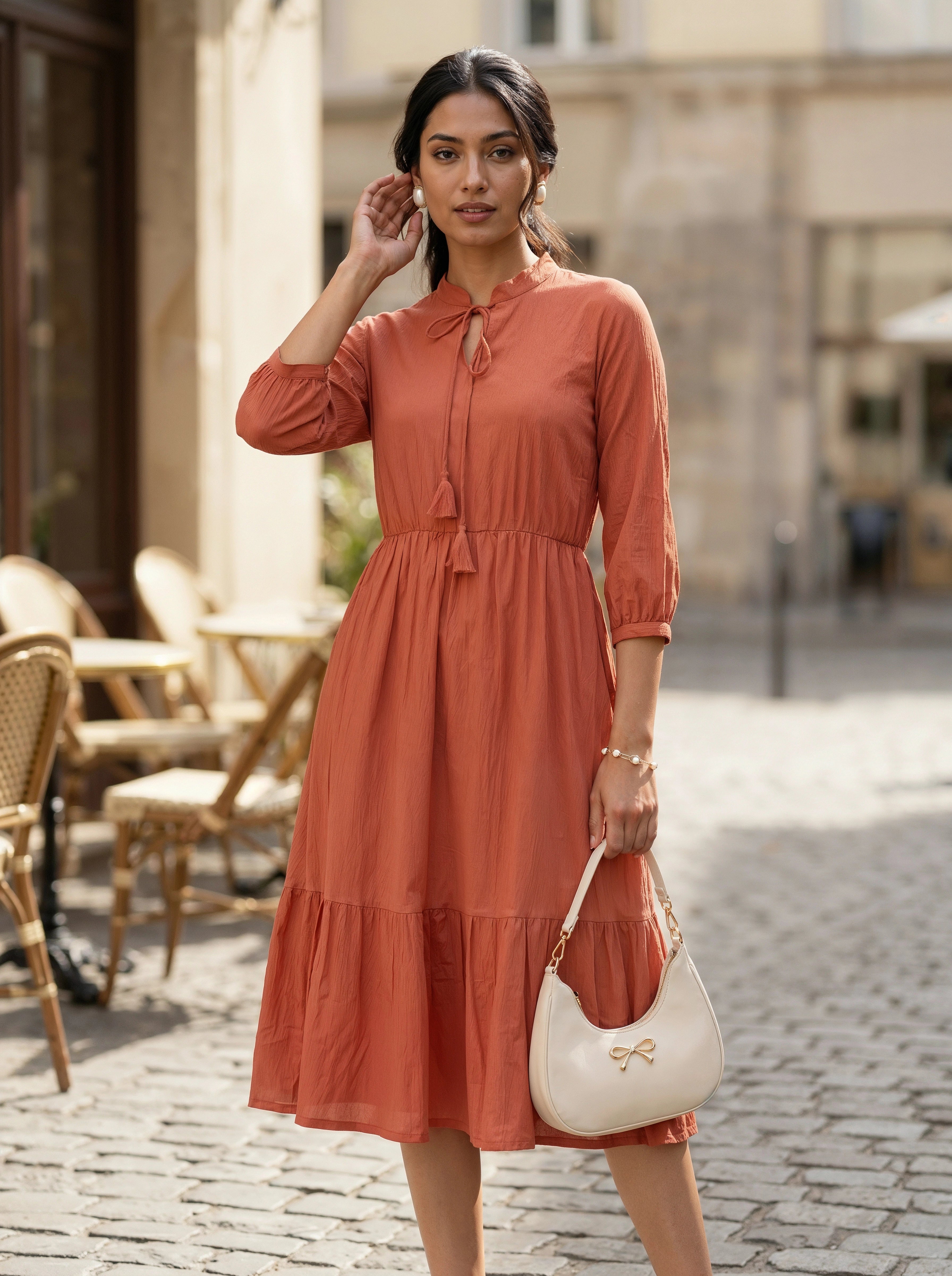 Woman in a rust-colored dress holding a white handbag on a street.