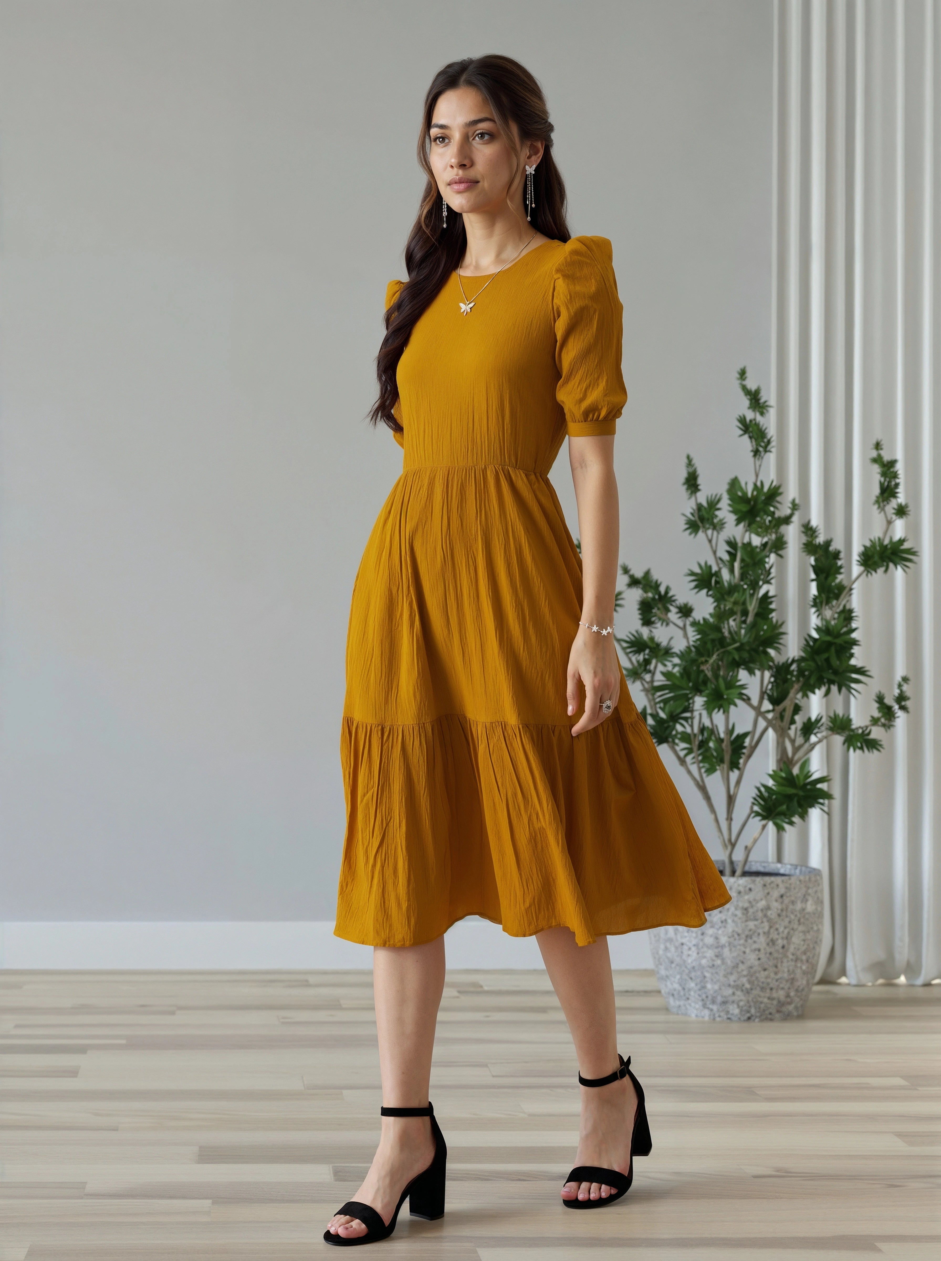 Woman wearing a mustard yellow dress standing in a room with a plant and light-colored walls.
