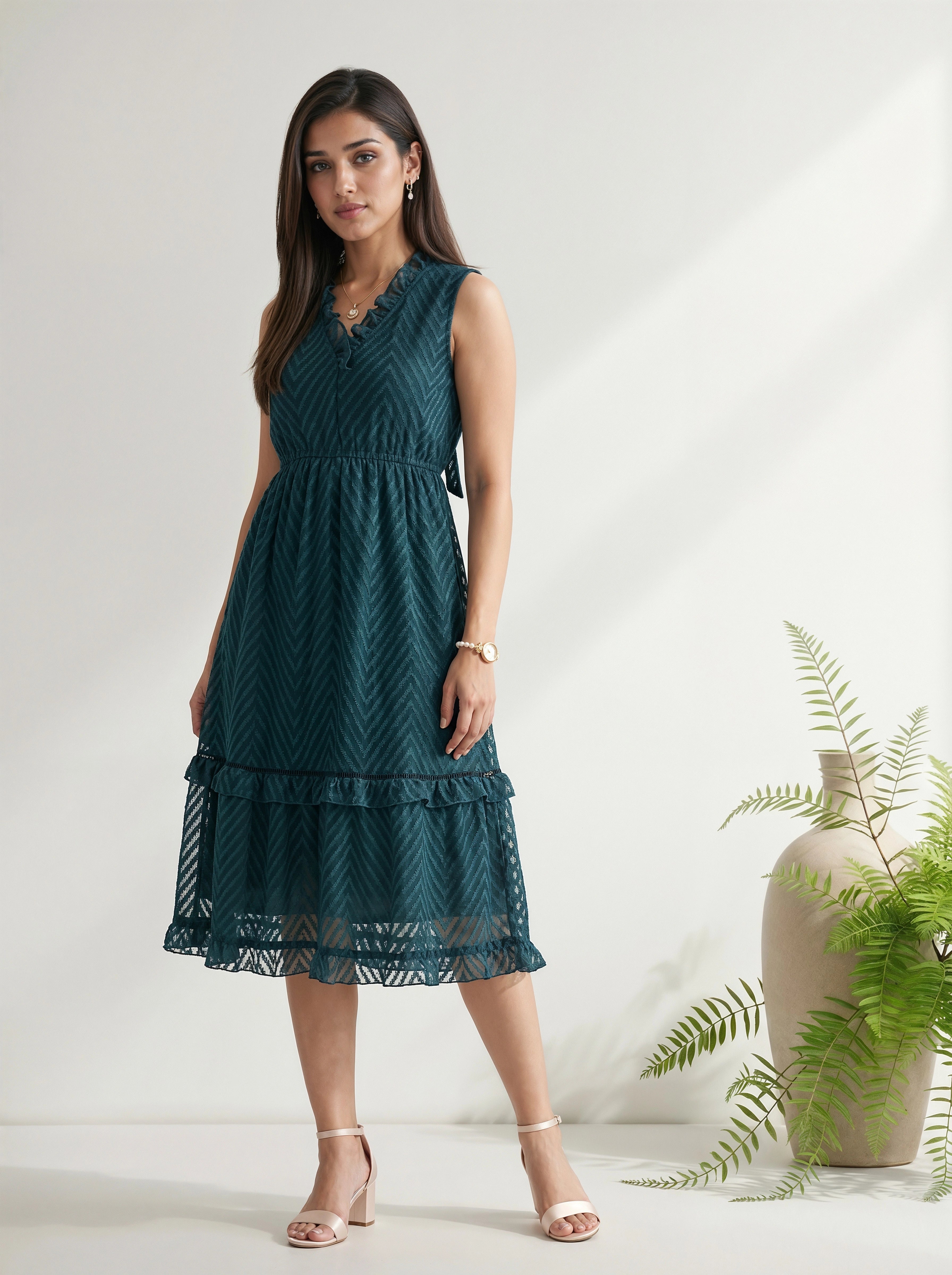 Woman wearing a dark green dress standing in a minimalistic setting with a plant.