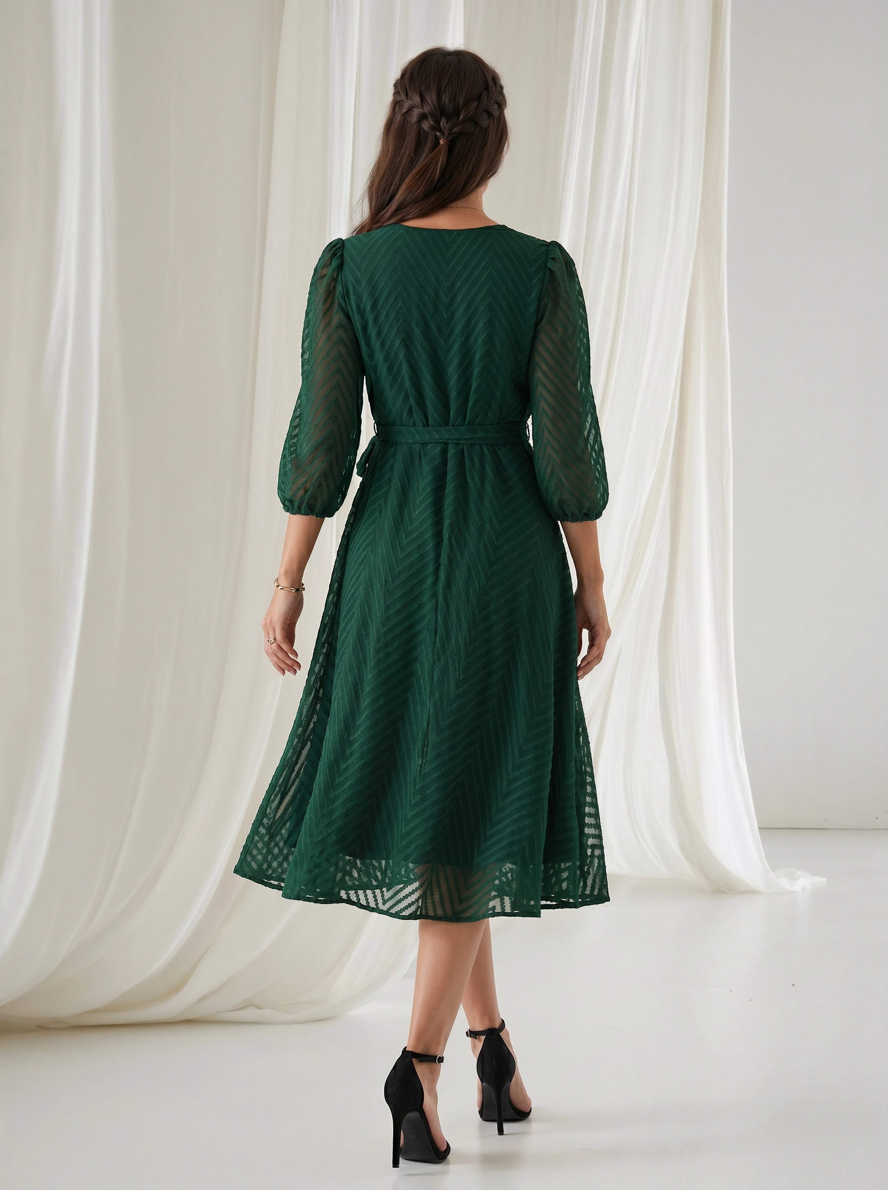 Woman wearing a green lace dress standing in front of white curtains.