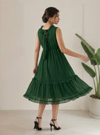 Woman wearing a green dress standing in a minimalistic room with a plant.