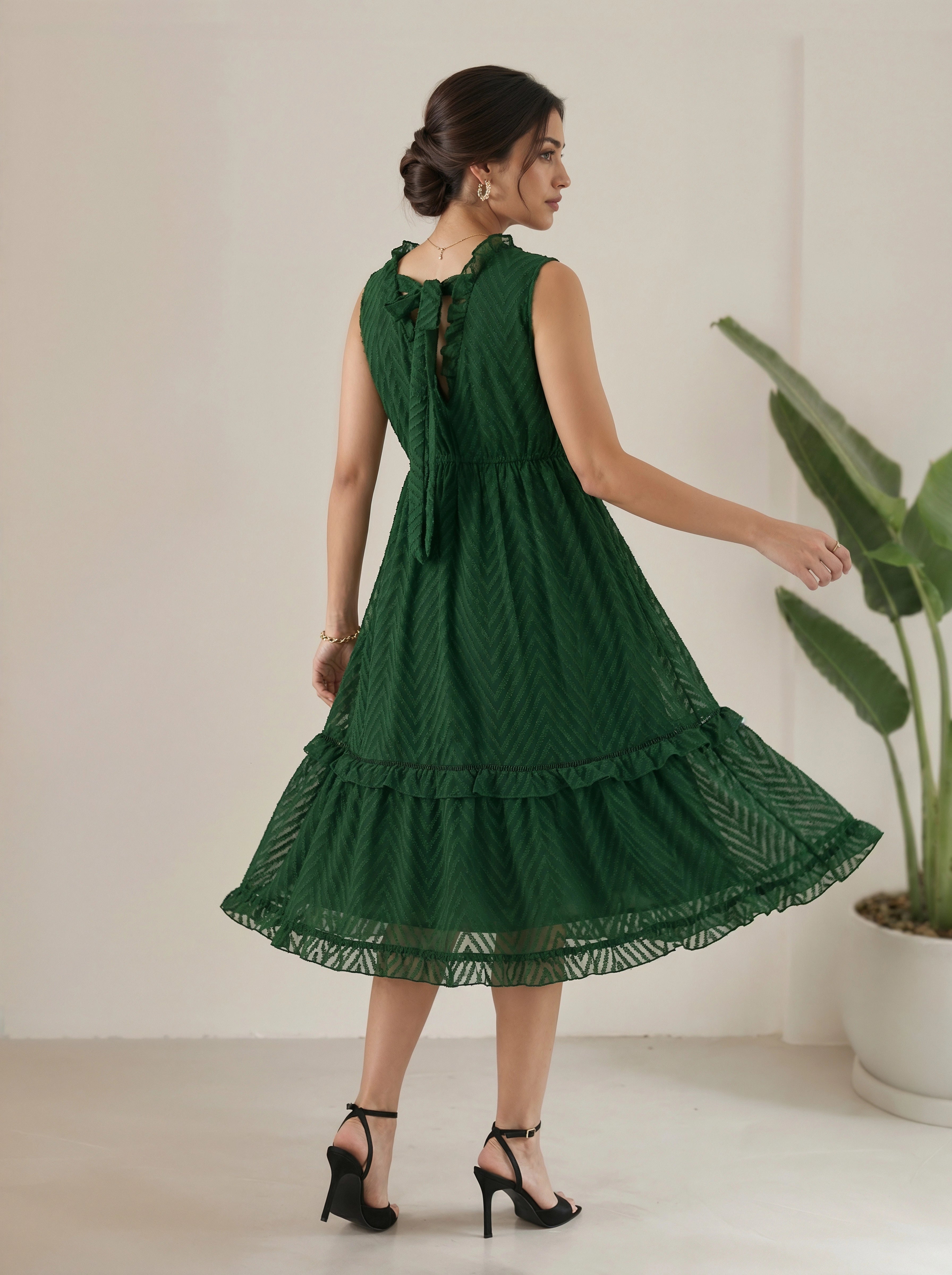 Woman wearing a green dress standing in a minimalistic room with a plant.
