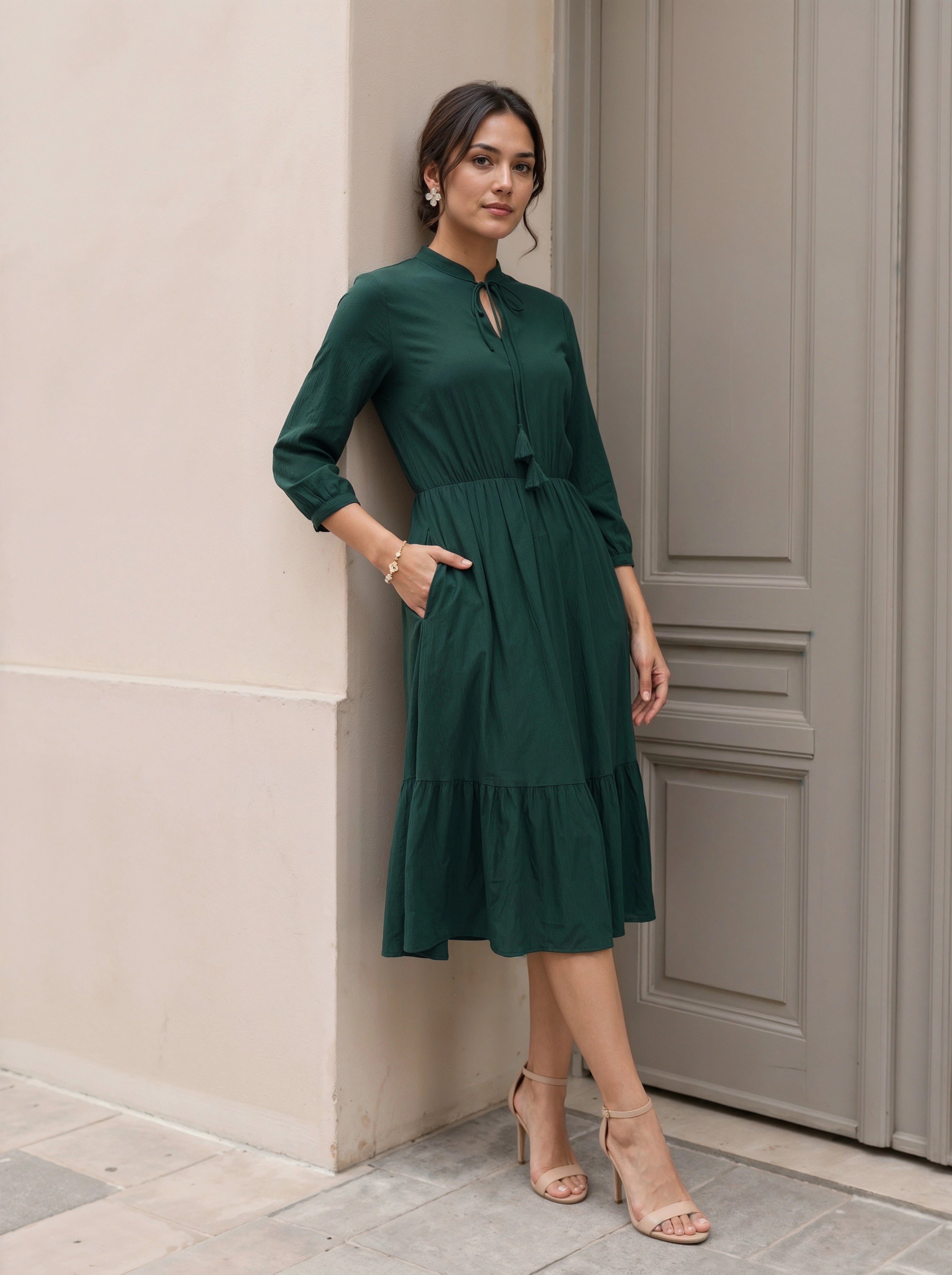 Woman in a green dress standing against a beige wall.