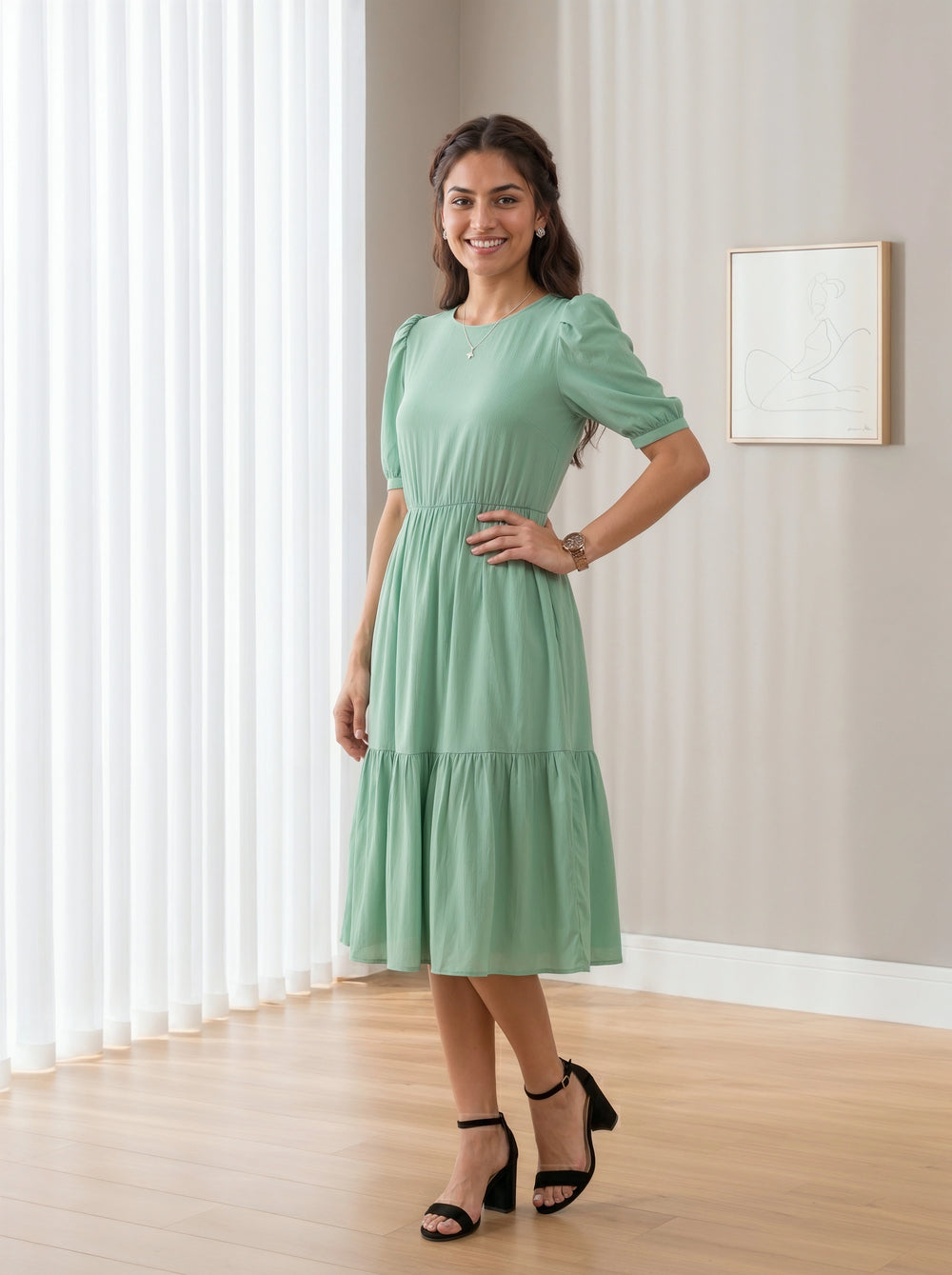 Woman in a green dress standing in a room with light-colored walls and wooden floor.