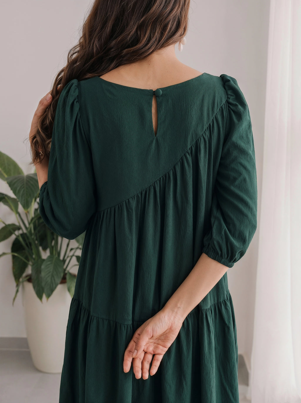 Woman wearing a green dress with long sleeves and a plant in the background