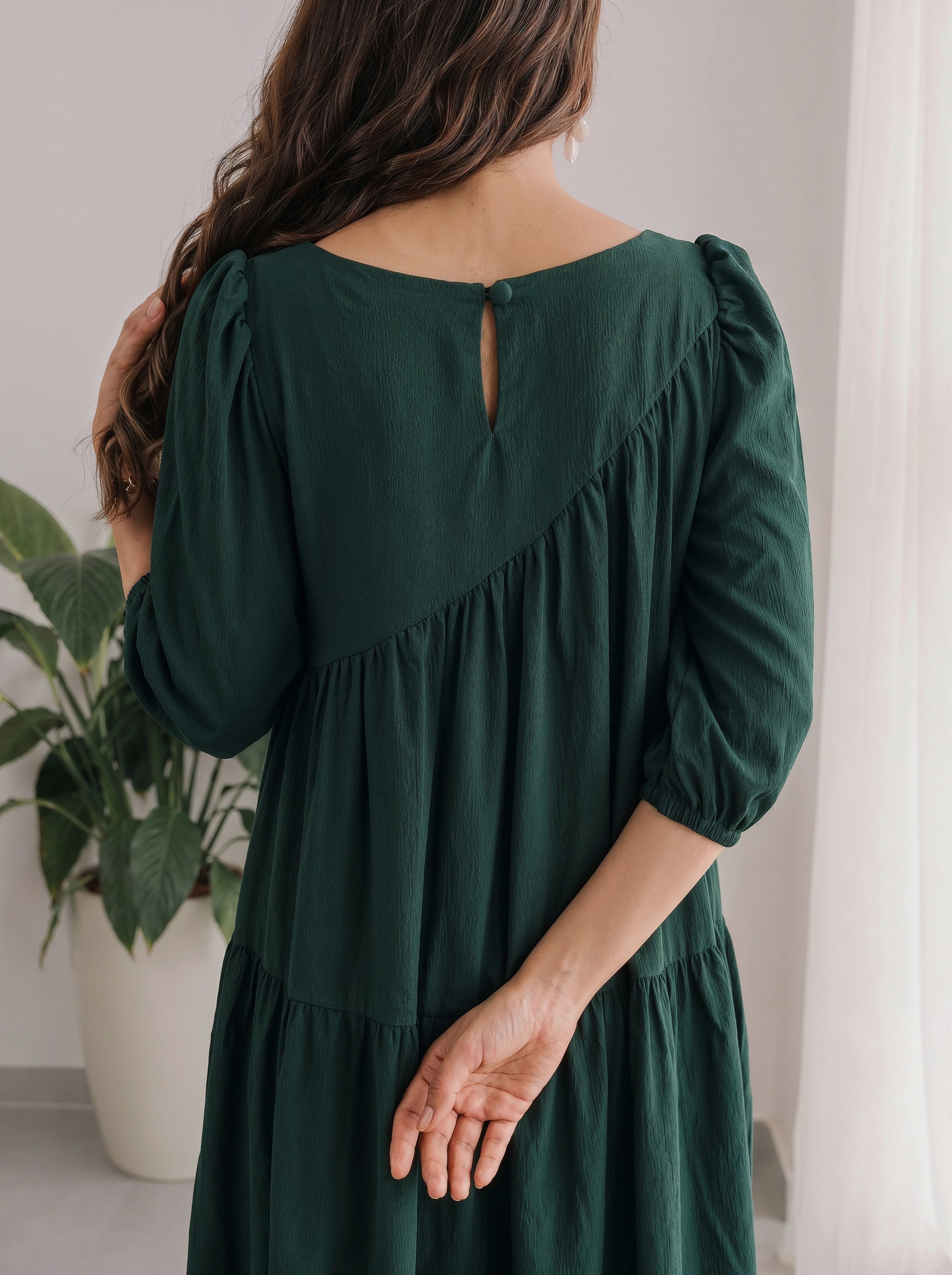 Woman wearing a green dress with long sleeves and a plant in the background