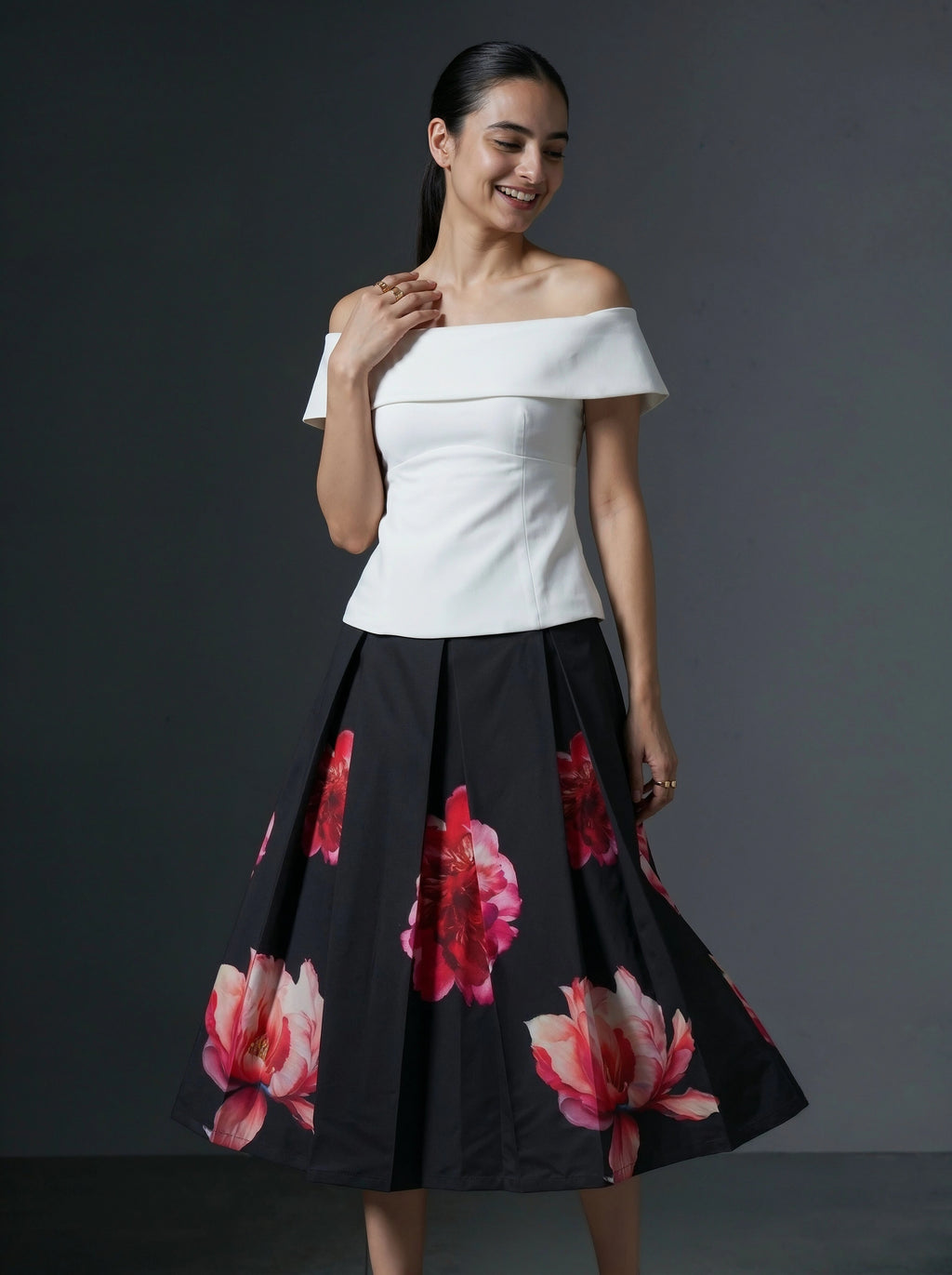 Woman wearing a white off-shoulder top and black floral skirt against a gray background