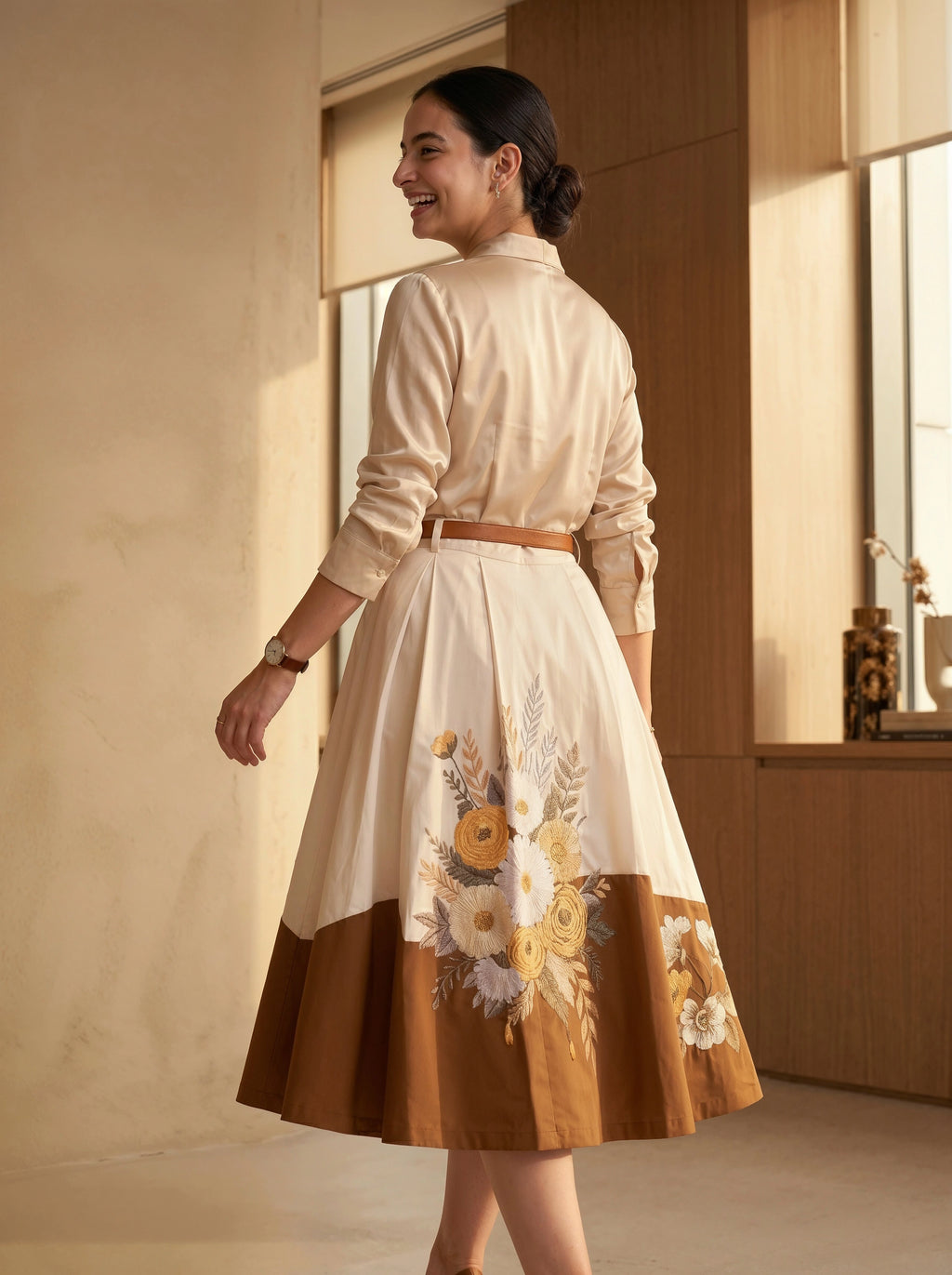 Woman wearing a cream blouse with a floral skirt in a warm-toned room.