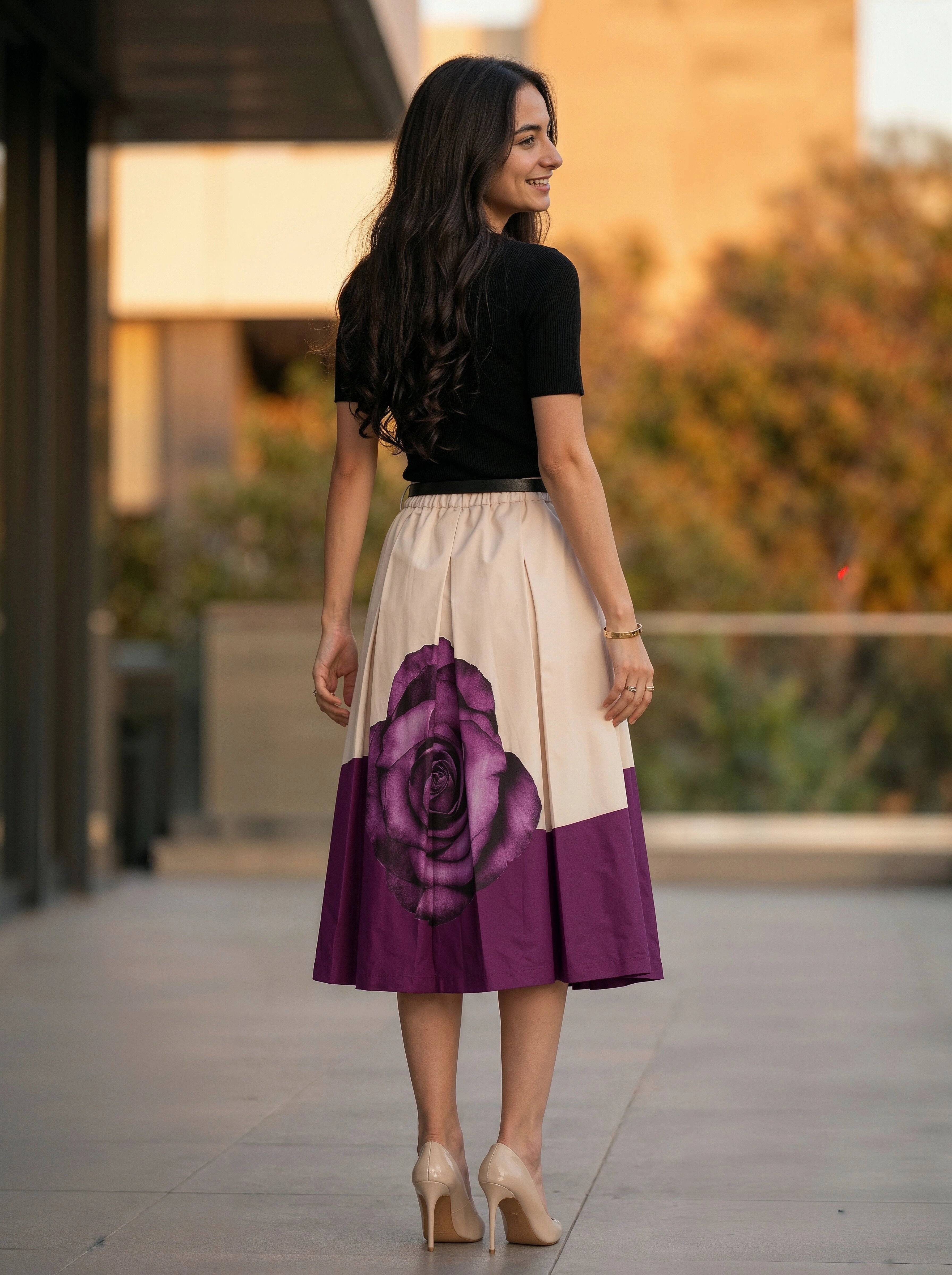 Woman wearing a black top and a skirt with a purple rose design, standing outdoors.