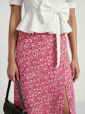 Person wearing a white peplum top and pink floral skirt with a black handbag.