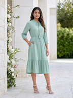 Woman in a light green dress standing outdoors with floral decorations.