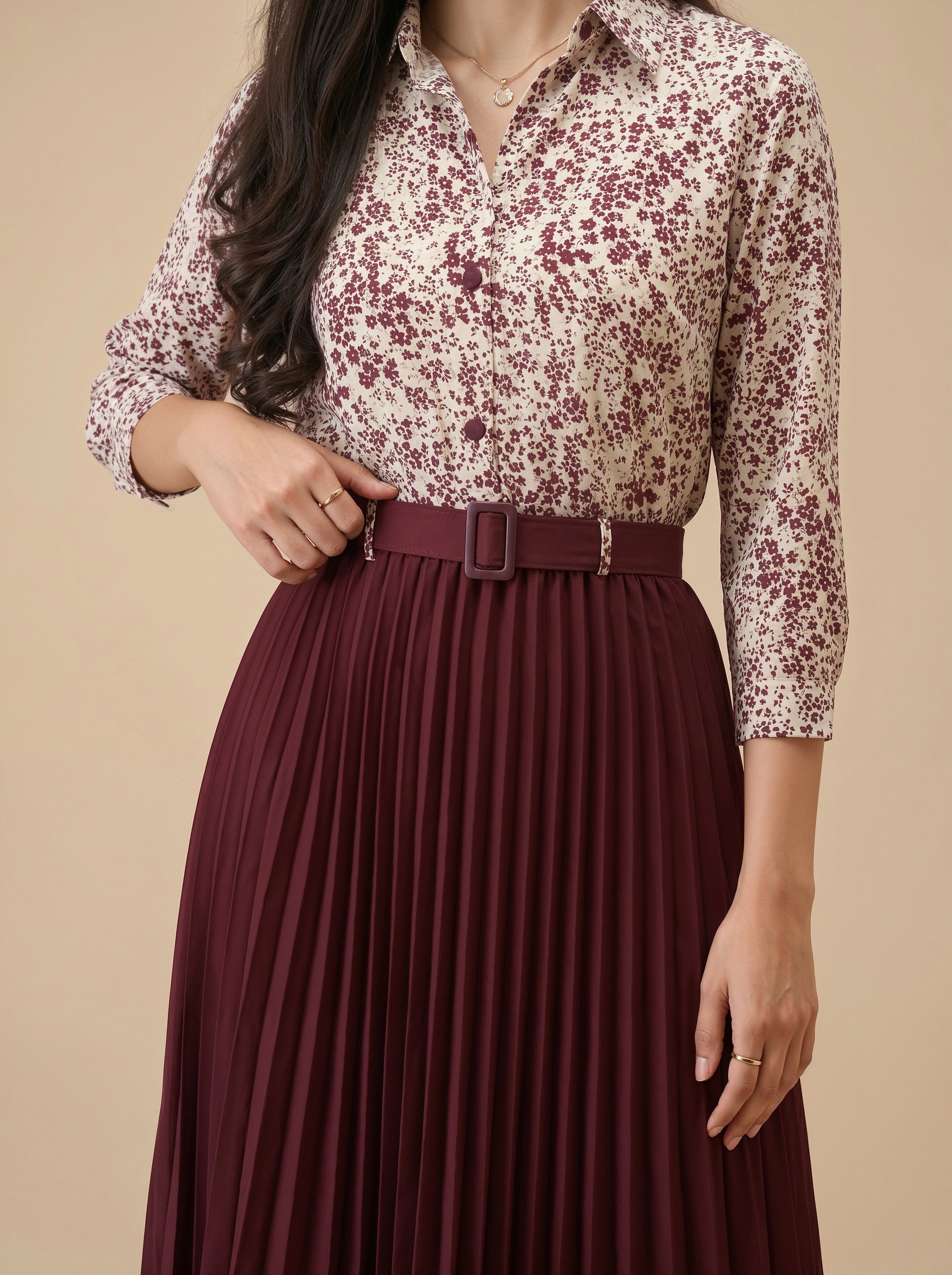 Woman wearing a floral blouse and burgundy pleated skirt on a beige background