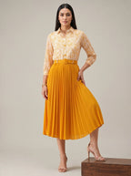 Woman wearing a yellow lace blouse and pleated skirt on a neutral background