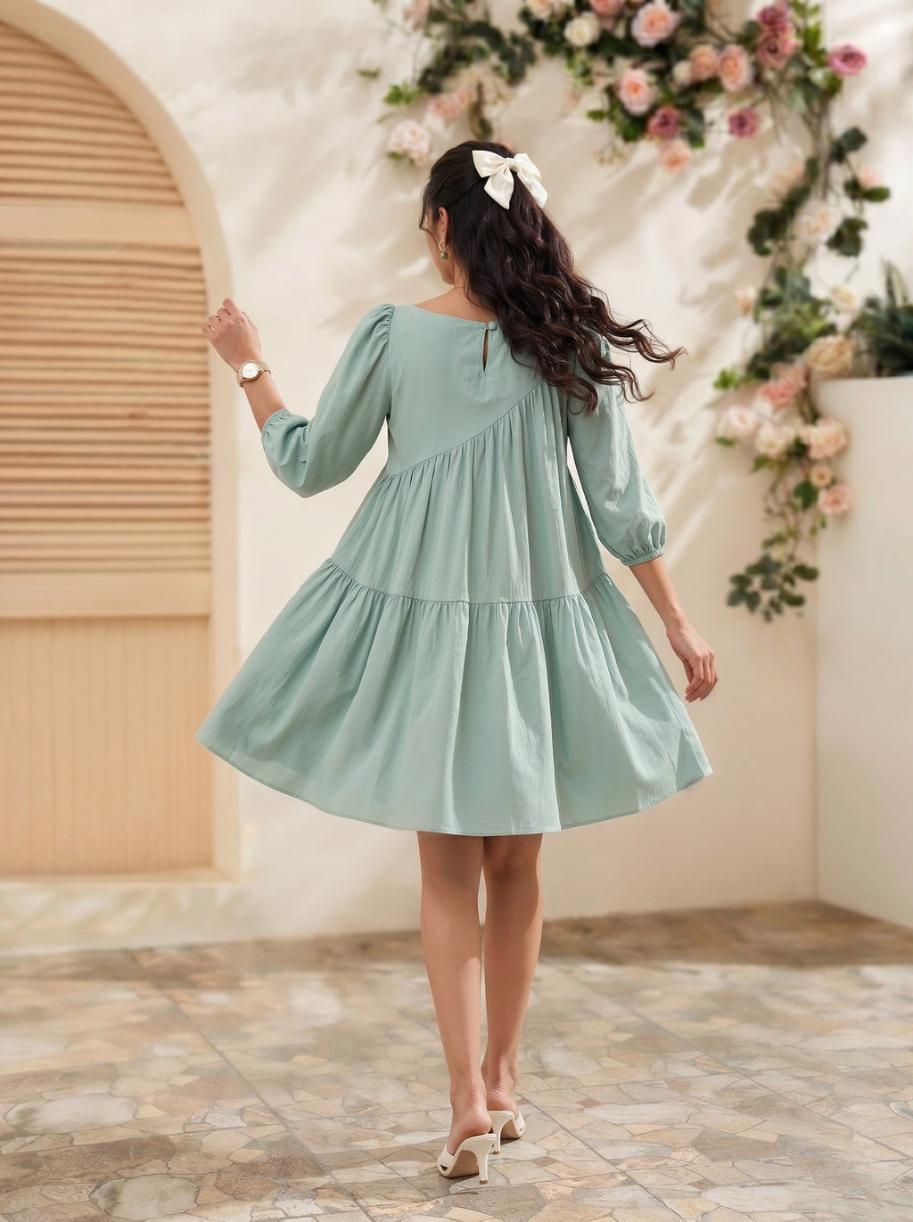 Woman in a light blue dress standing in a decorated indoor setting with flowers.