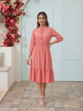 Woman in a coral dress standing in front of a floral wall and light blue door.