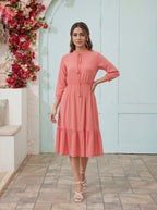 Woman in a coral dress standing in front of a floral wall and light blue door.