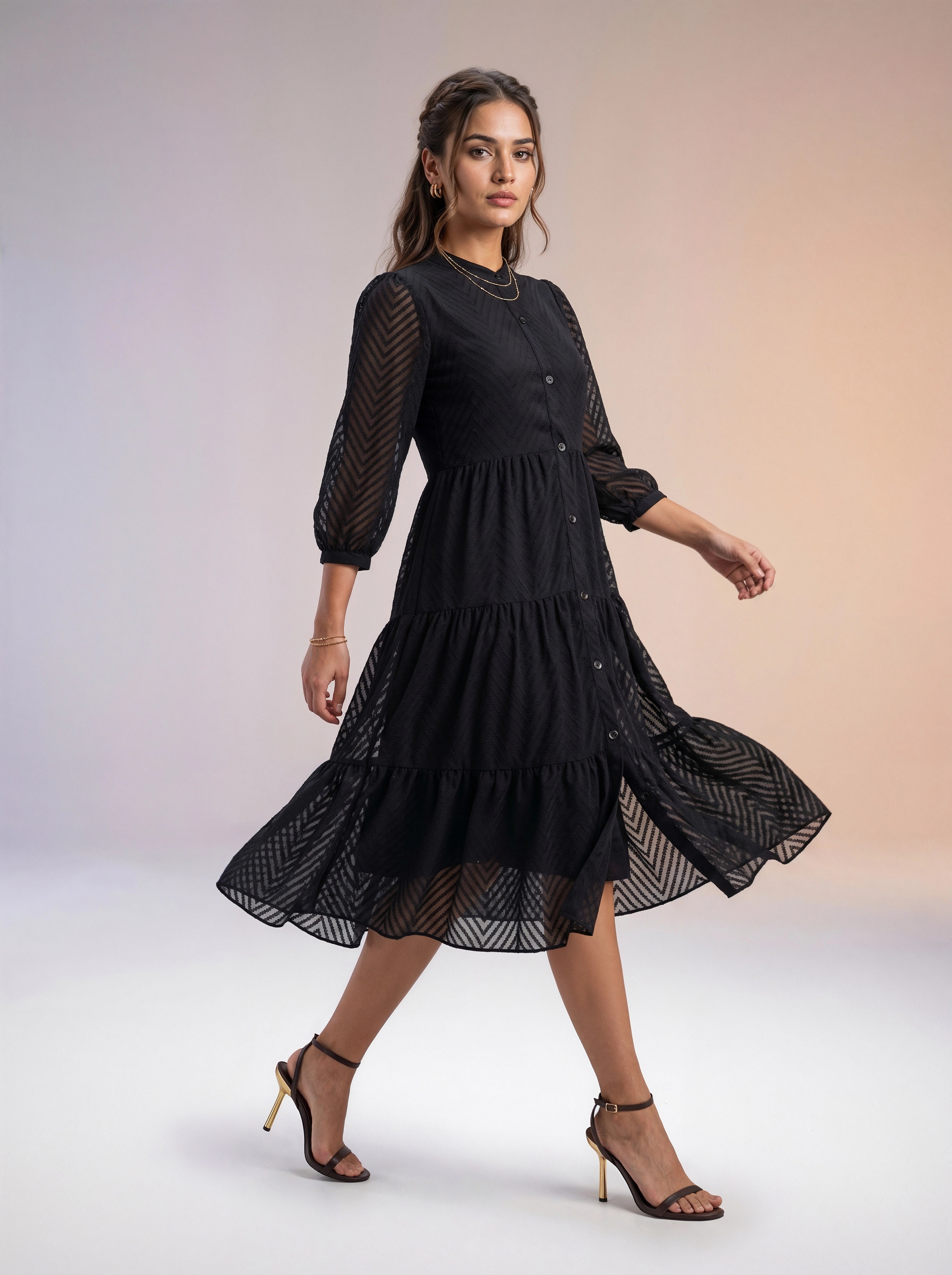 Woman wearing a black dress with sheer sleeves against a plain background
