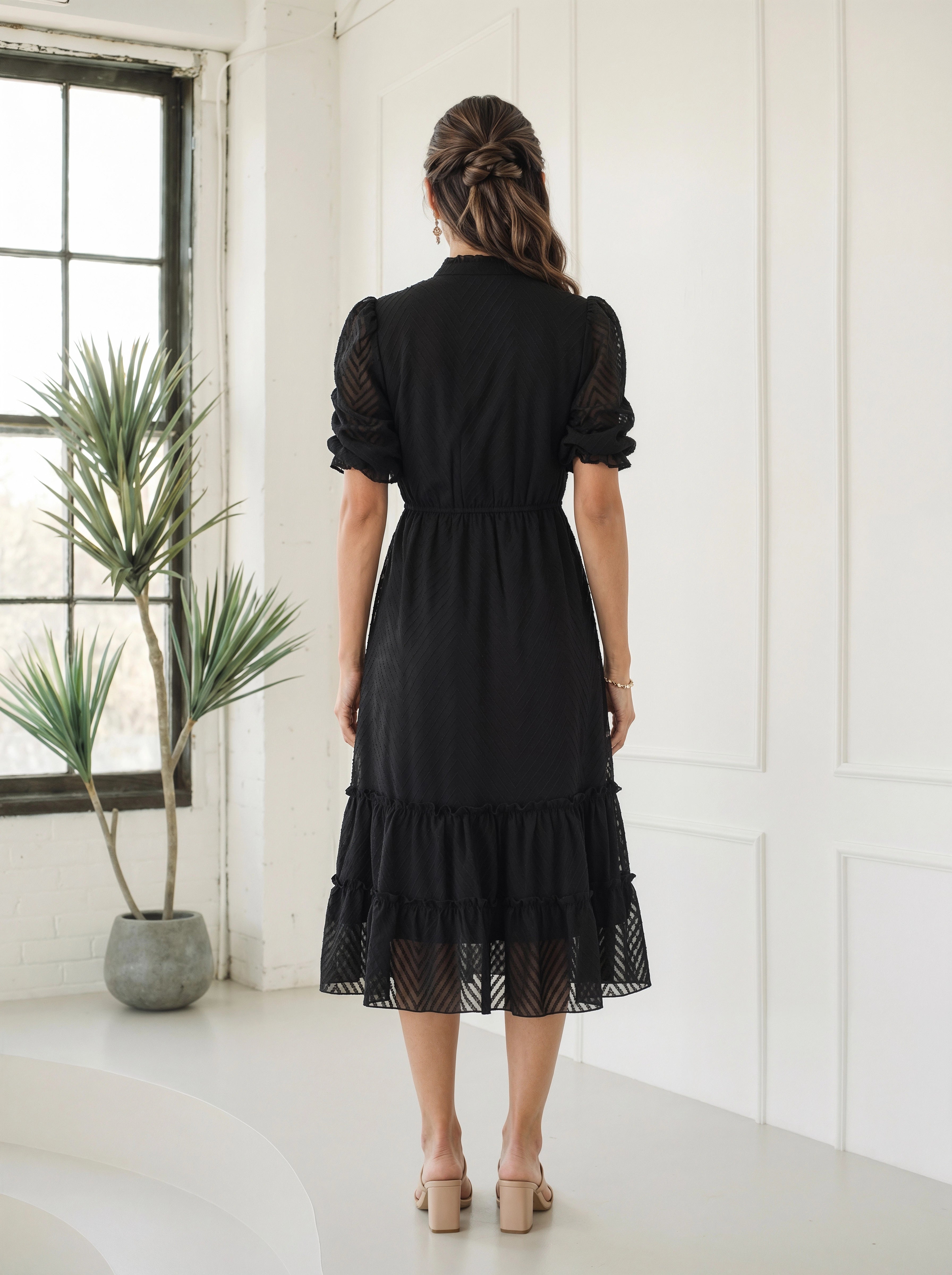 Woman wearing a flowy black tiered dress in a bright room setting